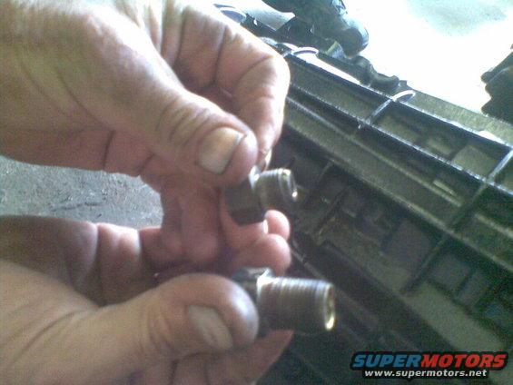 Two metal fittings held by hands, with a dark grille-like object in the background