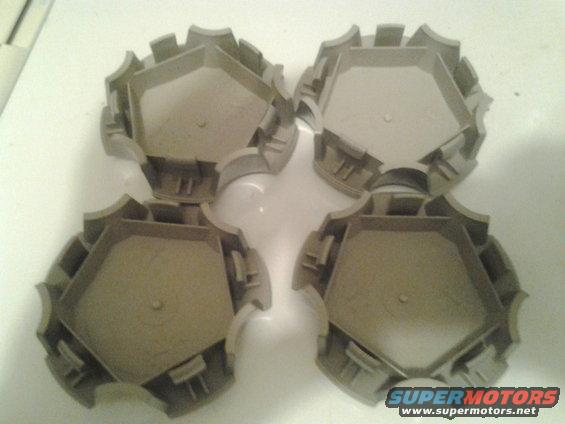 Four tan plastic hubcaps with a pentagonal center and a toothed outer edge
