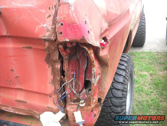 Red truck rear quarter panel, damaged taillight, exposed wiring, large tires
