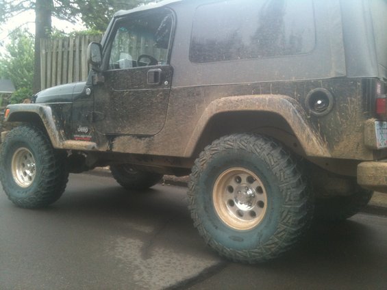 Mud-splattered black Jeep Wrangler Unlimited with gold rims and off-road tires, seen from the side