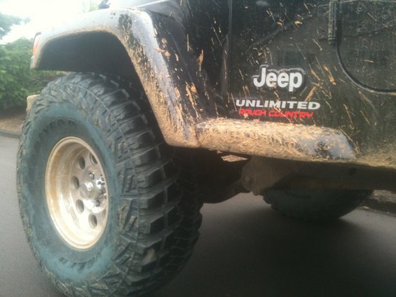 Mud-splattered black Jeep Wrangler Unlimited Rough Country side view, showing front tire and fender