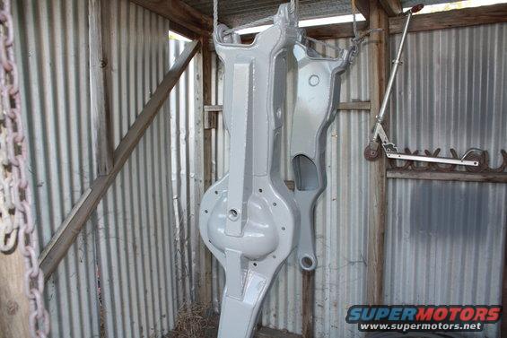 Gray painted axle assembly hanging in a shed. A scooter is mounted on the wall