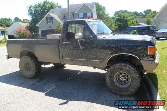 Mud-covered pickup truck parked on a street. It has large tires and a toolbox in the bed