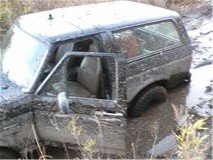 Mud-covered dark SUV, driver's door open, stuck in muddy water