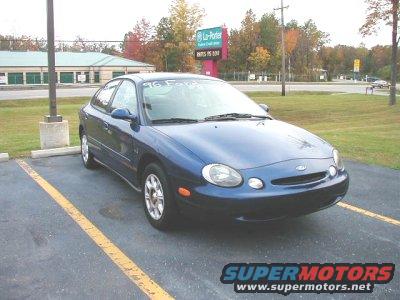 Blue sedan parked in a lot, windshield has '96 Ford written on it