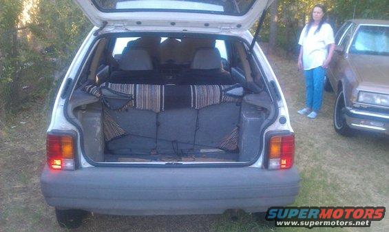 Rear of white hatchback with open trunk and striped interior fabric. Another car is parked to the right