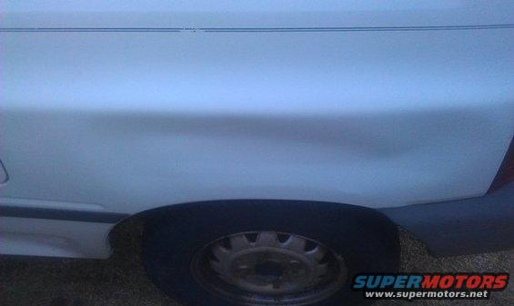 White car rear quarter panel with a dent above the wheel well and a black trim piece below