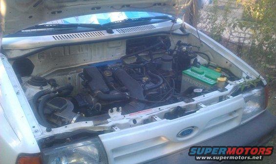 engine bay of a white car with hood open, showing engine, battery, and hoses