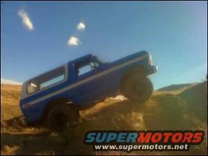 Blue and white SUV with white stripe climbing a dirt hill, front right wheel elevated