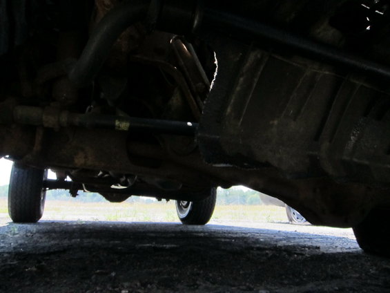 Underside view of a vehicle, showing suspension and drivetrain components. A tire is visible on the left