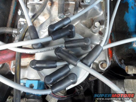 Close-up of a distributor cap with spark plug wires connected. Some wires have 'HI-TEMP SILICONE MADE IN' printed on them