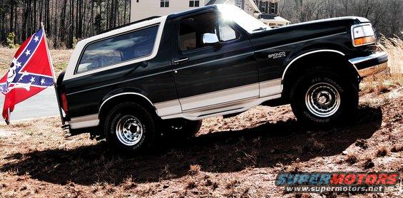 1993 Ford Bronco parked on a dirt incline with a Confederate flag attached to the rear bumper