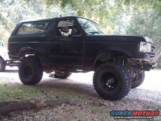 Lifted black 1989 Ford Bronco parked on gravel and grass