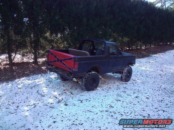 Dark blue Ford Bronco with a Confederate flag painted on its tailgate, parked in a snowy, wooded area