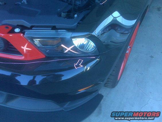 Black car front with red accents on the grille and headlight, marked with orange Xs and an arrow