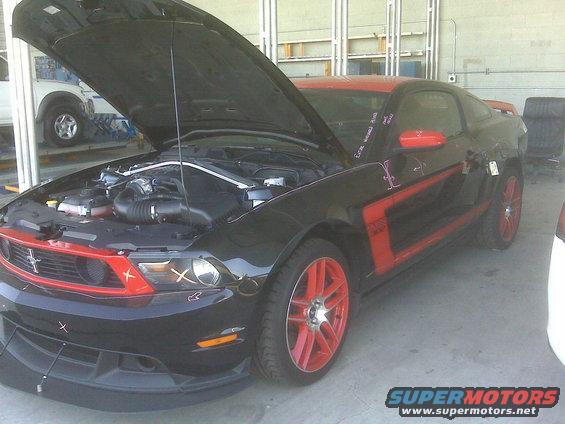 Black Ford Mustang with red accents and hood open, showing engine bay. Red wheels are visible