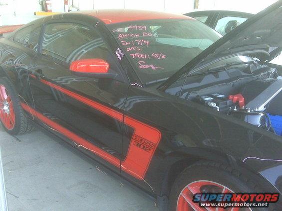 Black Ford Mustang Boss 302 with red racing stripes and red wheels, hood open, showing engine bay