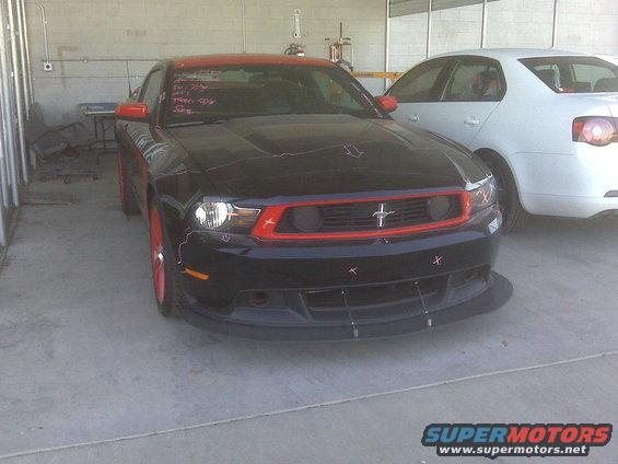 Black Ford Mustang with red grille and wheels, front view. Text on windshield