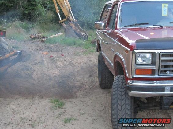 Red and tan Ford Bronco with large tires parked on dirt near an excavator