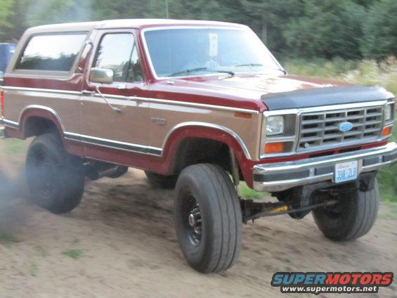 Red and tan Ford Bronco with lifted suspension and large tires, emitting smoke from the rear wheel