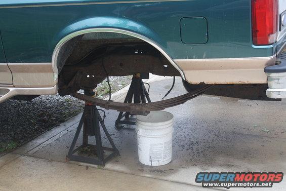 1996 Ford Bronco rear leaf spring removed and supported by jack stands, with a bucket underneath