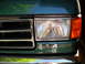 1990 Ford Bronco - Close-up of the front of a green 1990 Ford Bronco, showing the grille, headlight, and 4x4 badge.
