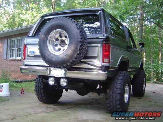 Dark green Ford Bronco rear view, lifted with large tires, spare tire on back, chrome bumper, dual exhaust pipes
