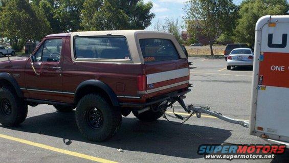 Maroon Ford Bronco with a tan removable top, towing a U-Haul trailer