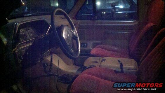 Car interior with red seats, a tan dashboard, and a steering wheel. The condition appears worn