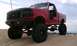 1994 Ford F-250 - A heavily modified red pickup truck sits on sand dunes under a cloudy sky.