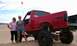 1994 Ford F-250 - A red 1994 Ford F-250 pickup truck is shown with a lifted suspension and large off-road tires, parked in a sandy area.