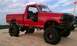 1994 Ford F-250 - A heavily modified red pickup truck sits on a sandy dune under a cloudy sky, with another vehicle visible in the distance.