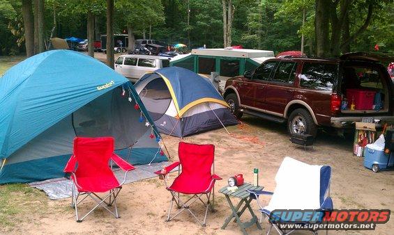 Maroon SUV with rear hatch open, parked next to tents at a campsite