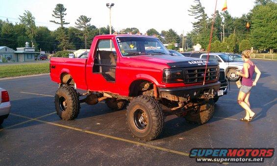 Red lifted pickup truck with doors removed, black grille, and hood decal reading 'GARAGE INC'