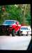 1994 Ford F-250 - A heavily modified red pickup truck is parked next to a white sedan on a paved surface with trees in the background.