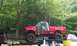 1994 Ford F-250 - A red pickup truck is loaded onto a trailer, partially covered by a tarp, with a dark SUV nearby.