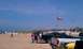 1994 Ford F-250 - People and trucks gather on a sandy beach under a clear blue sky with flags dotting the landscape.