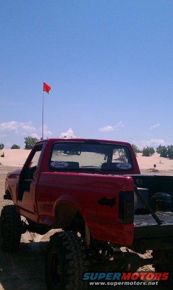 Red 1994 Ford F-250 with Ford decals on rear window, lifted with large tires, on sand dunes