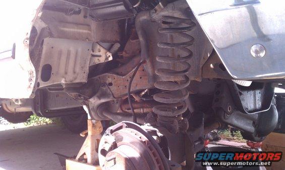 Front suspension and frame of a vehicle on jack stands, showing coil springs and brake rotor
