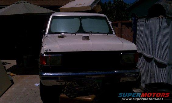Front view of a white Ford truck with a black grille and sunshades on the windshield. It's parked in a driveway with a patio umbrella and storage unit nearby