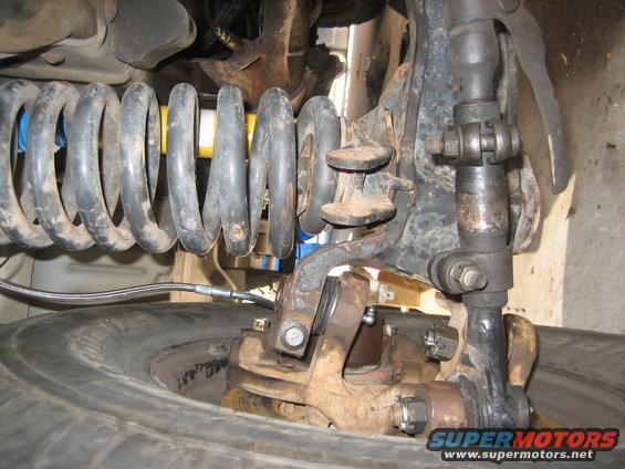Close-up of a vehicle's front suspension with a large coil spring, steering linkage, and tire visible
