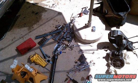 Mechanic's tools, including socket sets and wrenches, scattered on concrete next to jack stands and a toolbox
