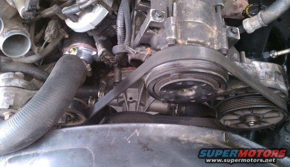 Engine bay with hoses, belts, and pulleys visible. Some components appear dirty