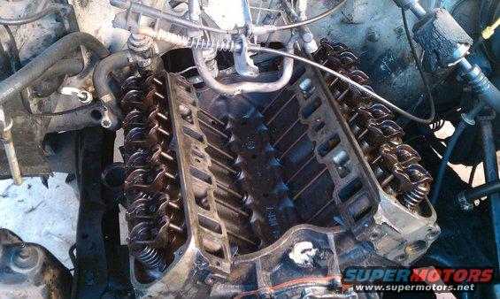 Engine block with valve covers removed, showing rocker arms and springs. Some hoses and wiring are visible