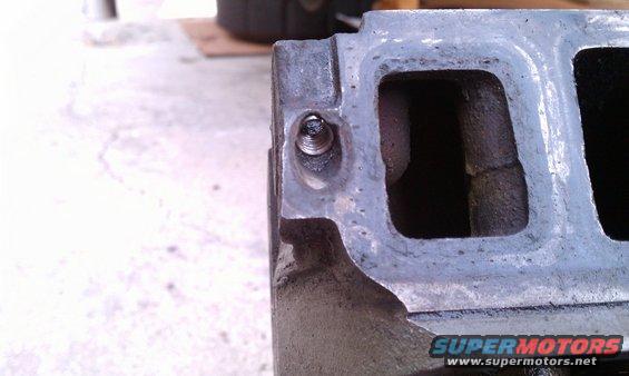 Close-up of a metal engine intake manifold with a bolt in one of the ports