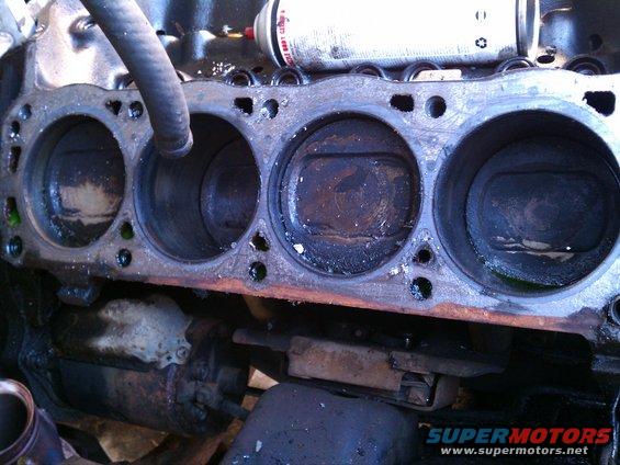 Engine block with four visible pistons, showing carbon buildup and wear