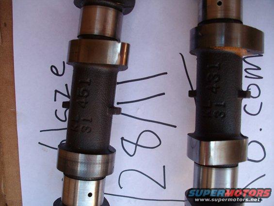 Two camshafts with part numbers stamped on them, lying on paper with handwritten markings