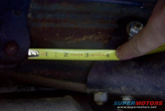 Tape measure on a rusty metal part, possibly suspension. Hand holding tape measure near the 4-inch mark