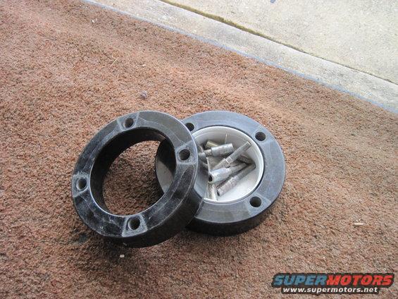 Two black circular automotive parts, one containing small metal pins, lie on a brown carpet