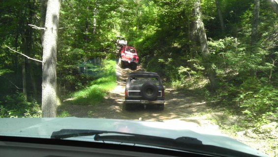 Black 1989 Ford Bronco rear view on forest trail with other vehicles